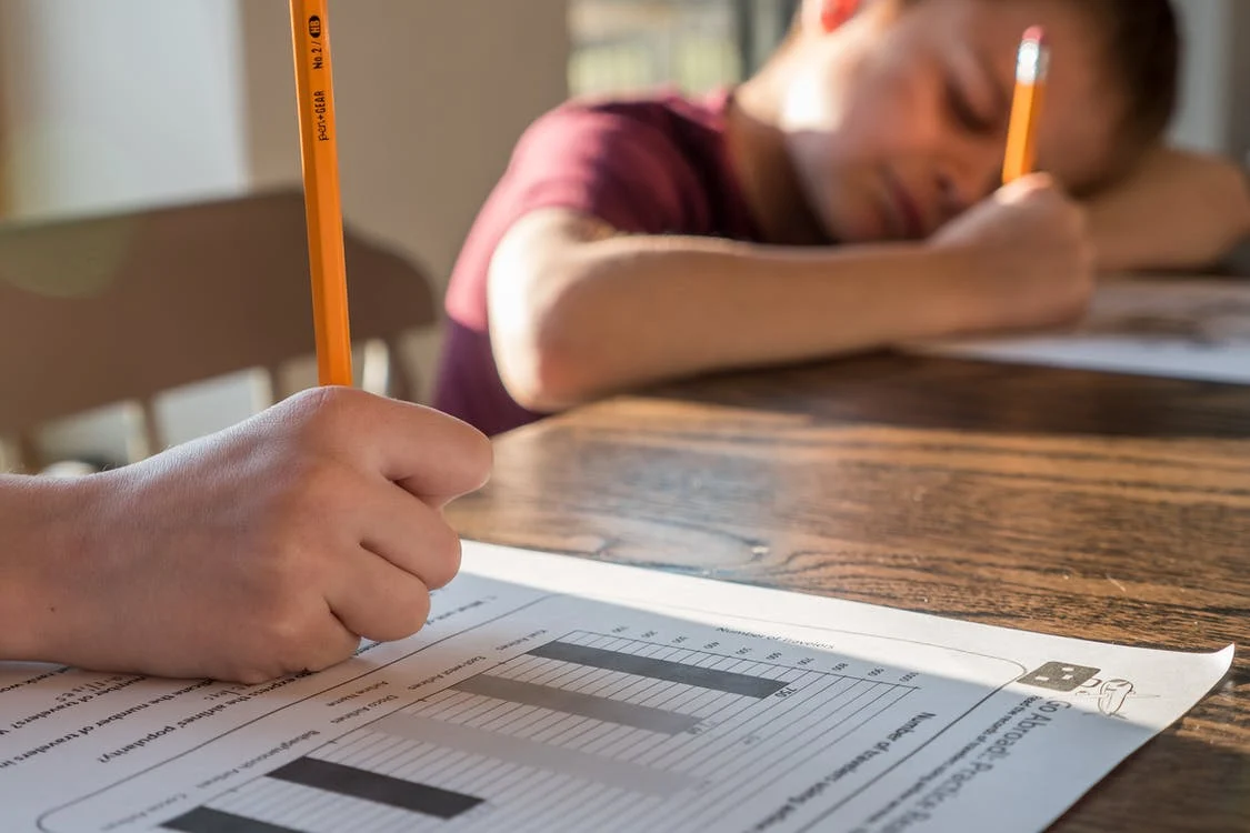 This image shows two young kids using their yellow colored pencils to write on the practice papers.
