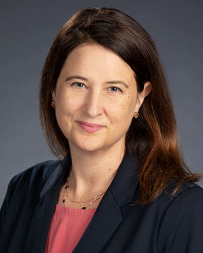 This is a close-up image of a woman named Stephanie Cawthon. She is wearing a black formal jacket with a reddish pink top inside.