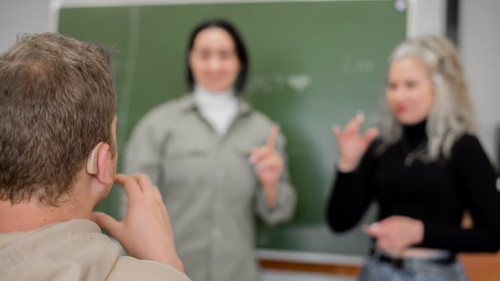 Dos chicas y un chico están hablando en lenguaje de señas. Tres estudiantes sordos charlando en un aula universitaria