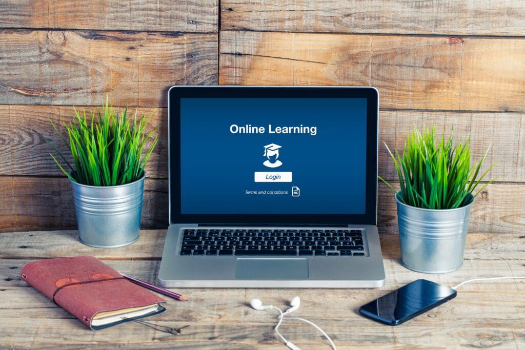 Laptop and a plant placed on a table. The laptop screen displays "Online Learning" and "Login" with "Terms and conditions" below.