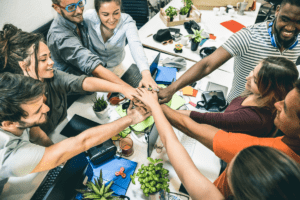 Grupo de personas reunidas alrededor de una mesa, sonriendo y compartiendo. Las personas llevan varios tipos de ropa y parecen estar participando en una actividad social.