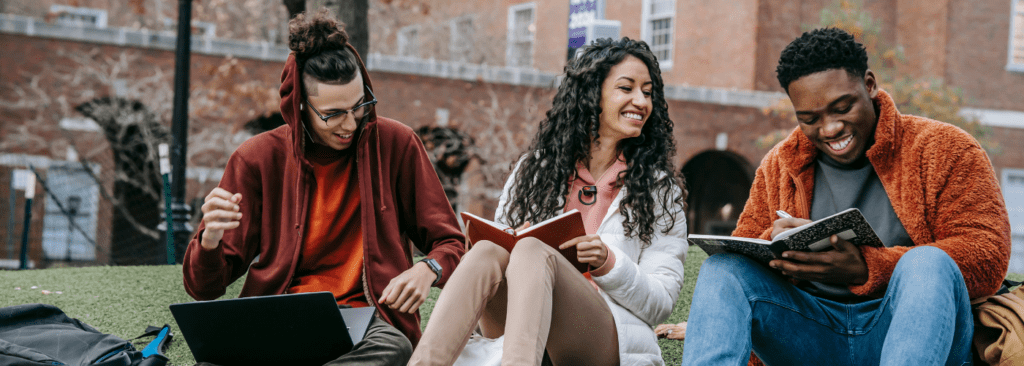 Grupo de personas sentadas al aire libre leyendo un libro y riendo.