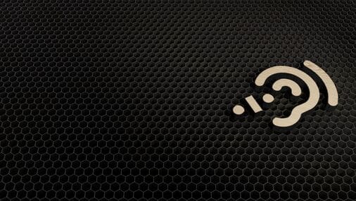 The image features a dark, hexagonal patterned background reminiscent of a honeycomb texture, predominantly in shades of black. Positioned towards the right side of the image is a beige or light-colored icon that resembles an ear with sound waves, symbolizing hearing or audio. 