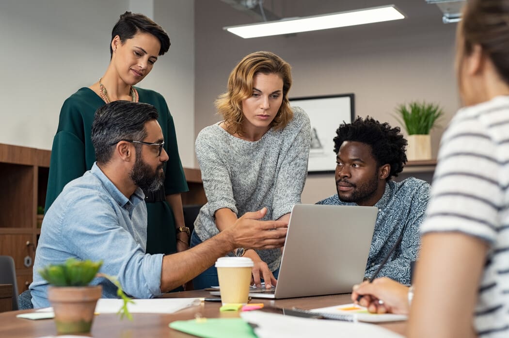 Diverse team collaborating around a laptop in a modern office, discussing project ideas.